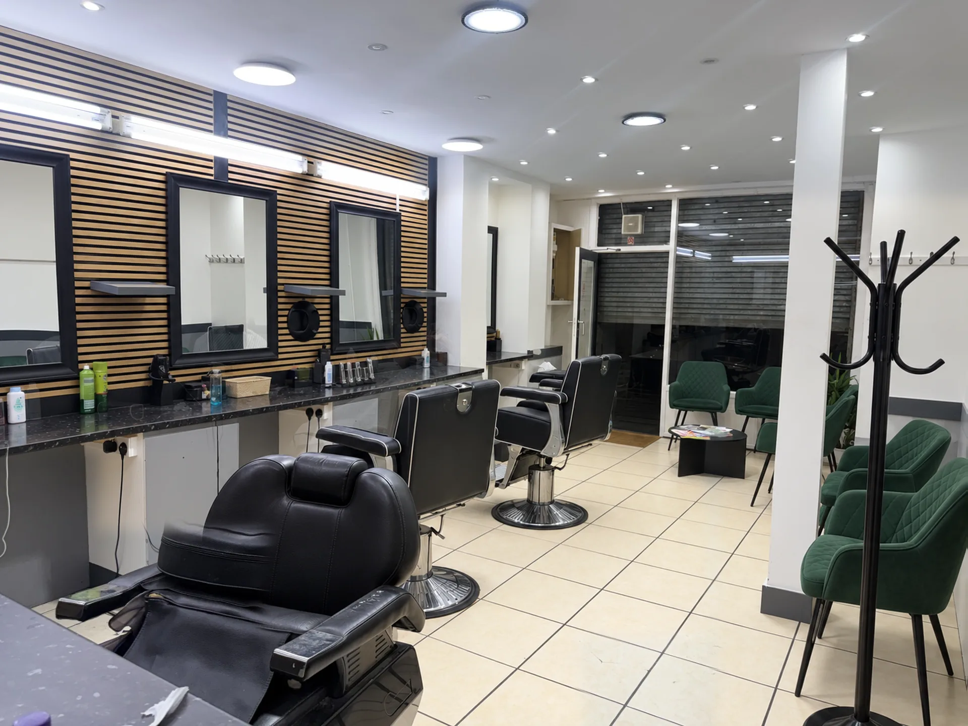 Inside Iqbal Gents: black barber chairs, black-framed mirrors on an oak slat wall and green velvet waiting chairs
